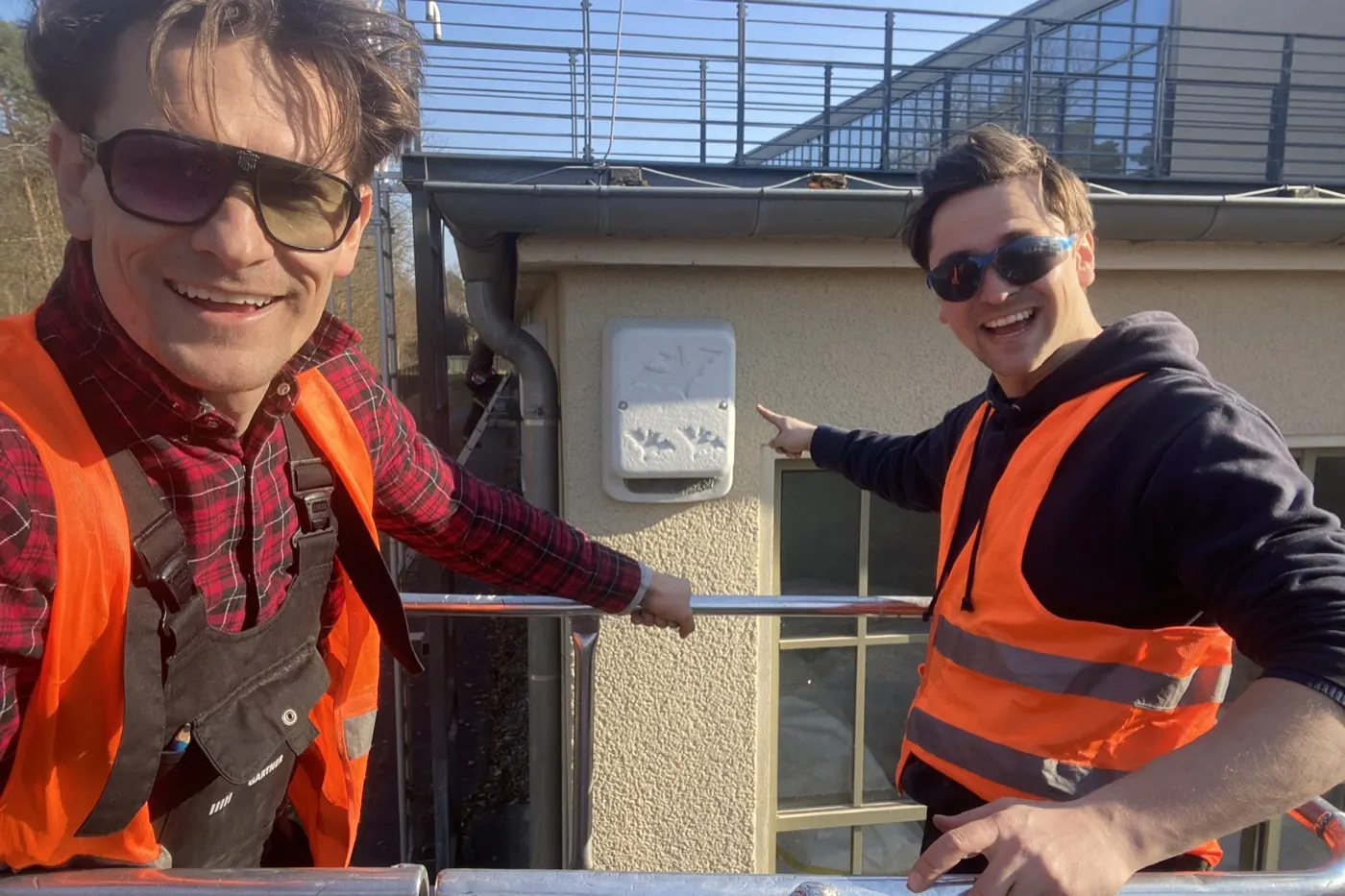 Zwei Baumpfleger auf der Hebebühne zeigen auf einen Fledermauskasten an der Fassade