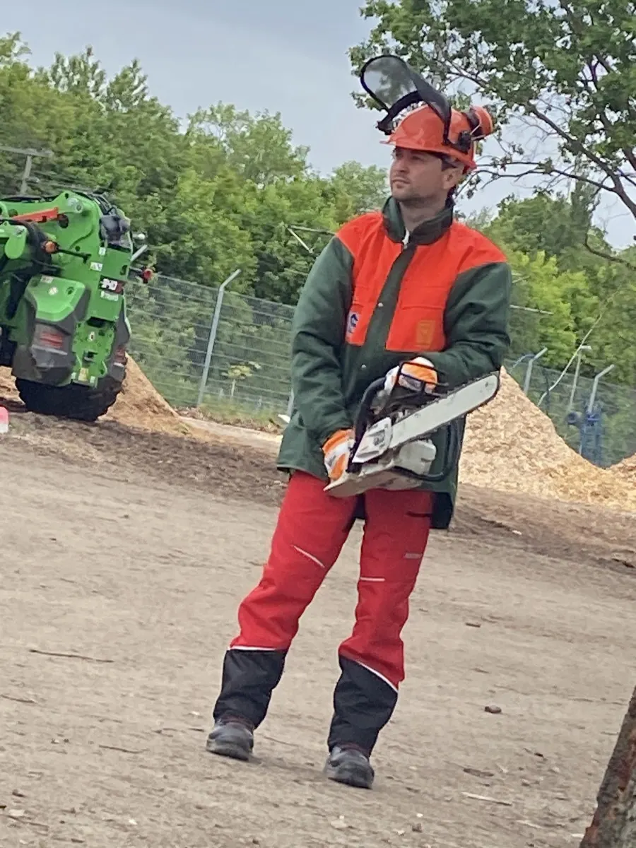 Baumpfleger in Schnittschutzkleidung und Helm mit Motorsäge auf einem Betriebshof